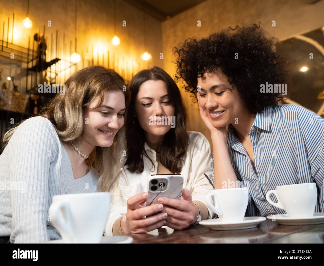 Groupe de diverses amies féminines naviguant sur smatphone dans un café Banque D'Images