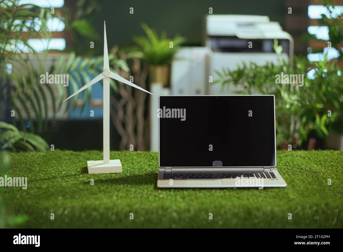 Tendances écologiques. bureau en herbe dans un bureau vert moderne avec ordinateur portable, écran vierge et moulin à vent. Banque D'Images