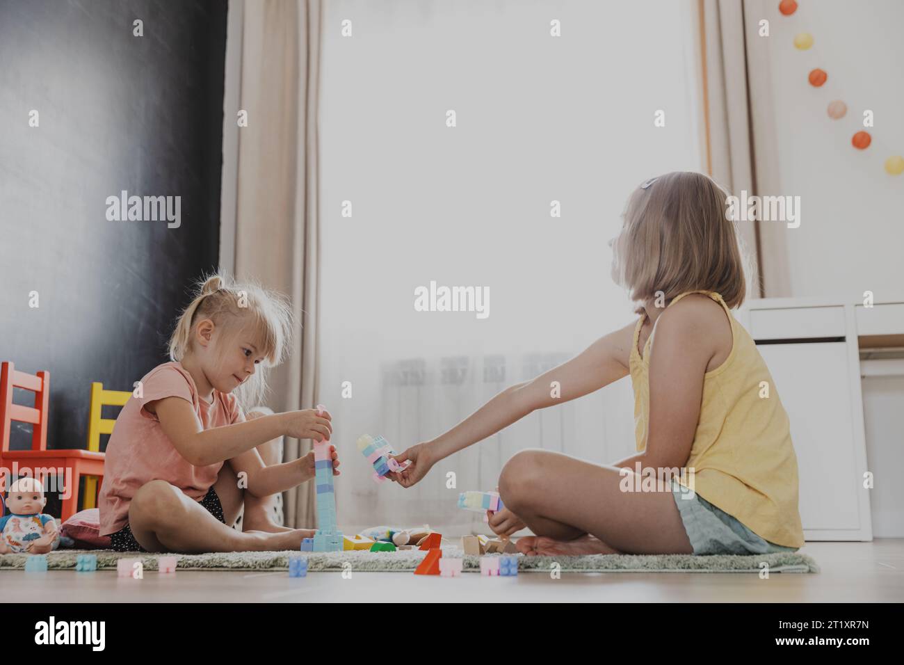 Enfants jouant avec des blocs de construction de constructeur colorés, des briques. Enfants assis sur le sol à l'intérieur à la chambre à coucher blanche ensoleillée ou à la maternelle, centre de jeux. Jeu éducatif amusant pour enfants respectueux de l'environnement Banque D'Images