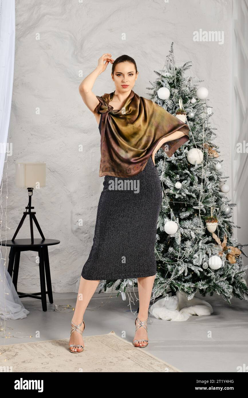 Jeune femme en robe noire serrée avec paillettes et foulard en soie posant près de l'arbre de Noël Banque D'Images