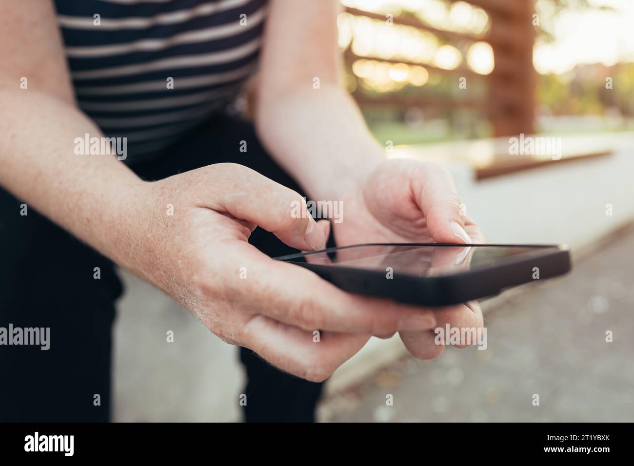 Gros plan des mains féminines messagerie texte sur smartphone sur banc de parc public, mise au point sélective Banque D'Images