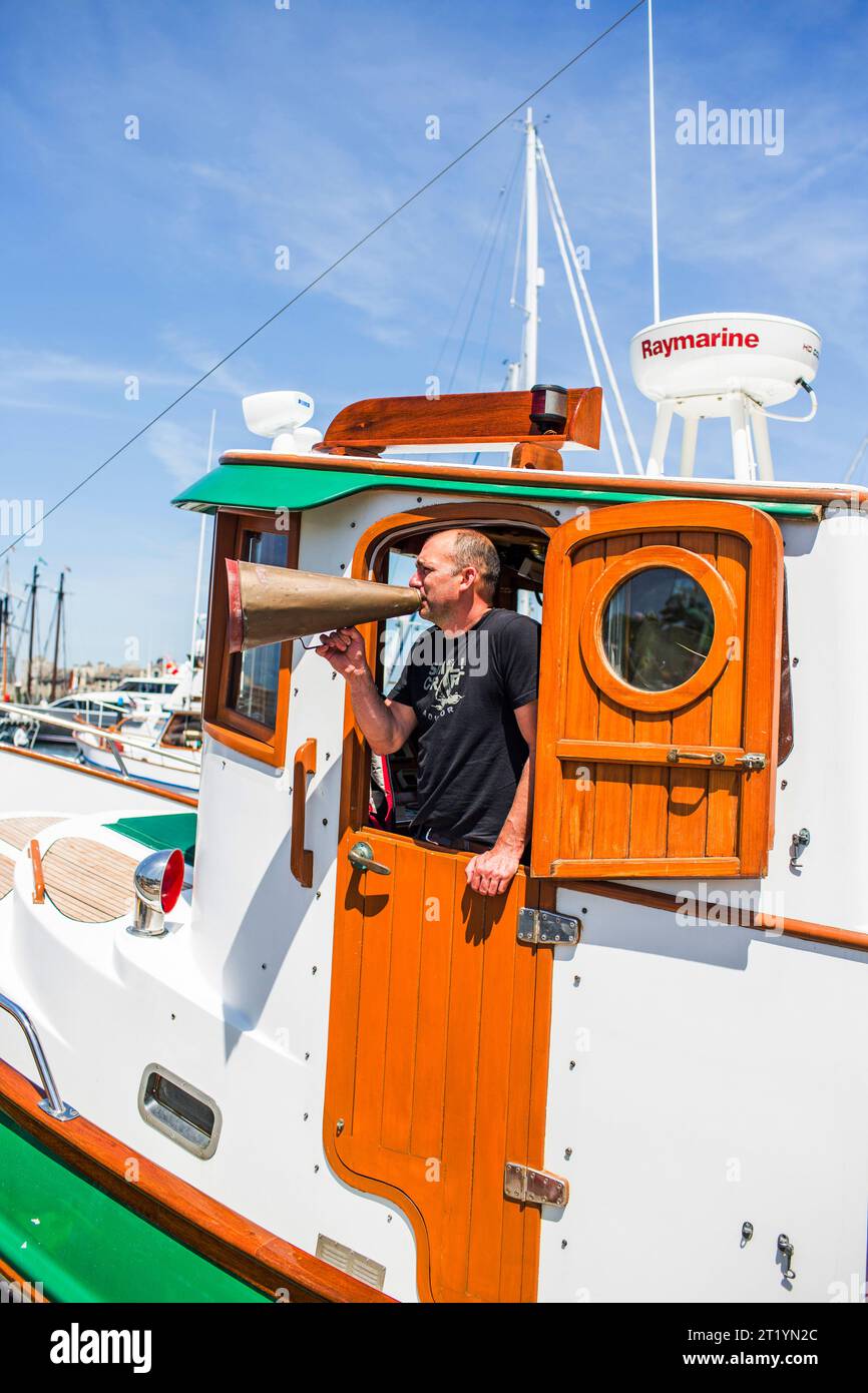 Le fondateur de la course en Alaska se tient sur un bateau de soutien avec un mégaphone à Victoria pendant la course en Alaska. Banque D'Images