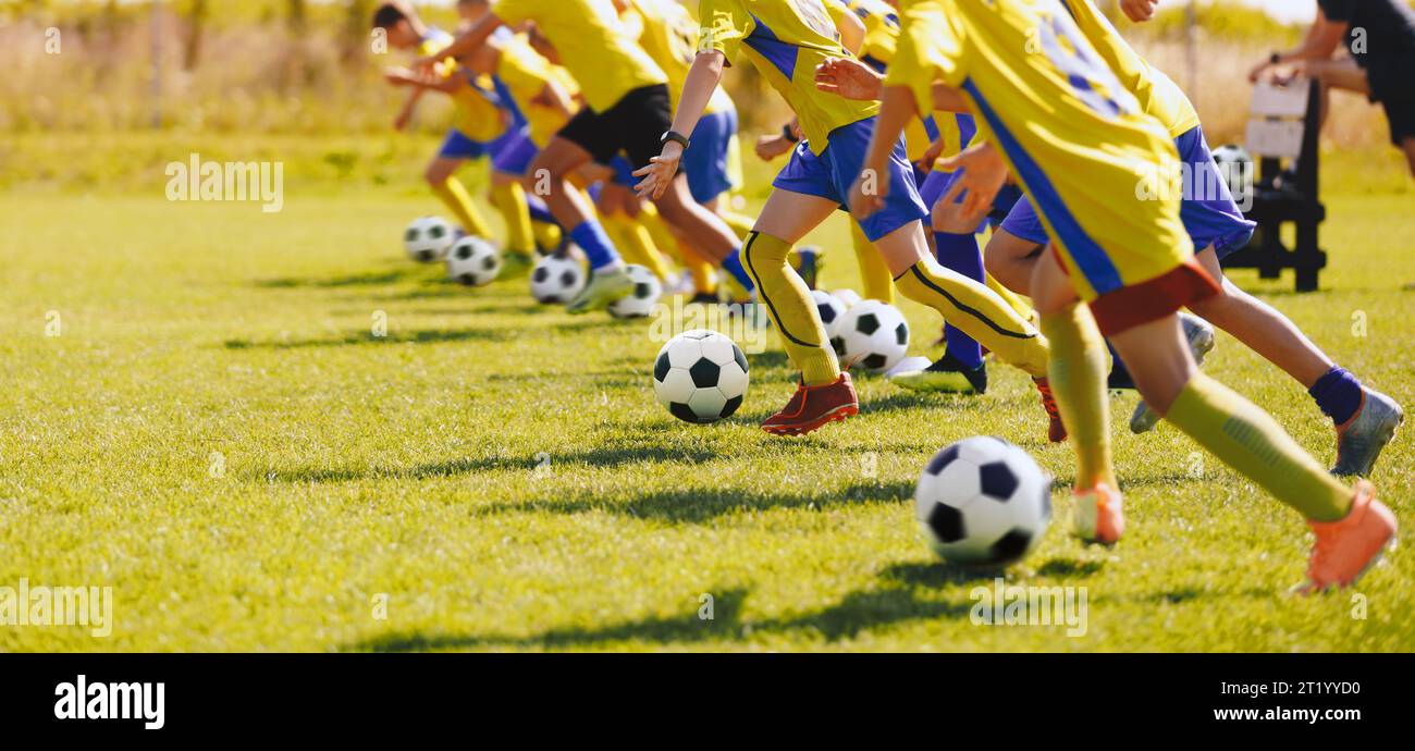 Football football joueurs juniors en classe d'entraînement. Garçons pratiquant le football sur un terrain d'herbe. Groupe d'écoliers qui courent et frappent des ballons de soccer Banque D'Images