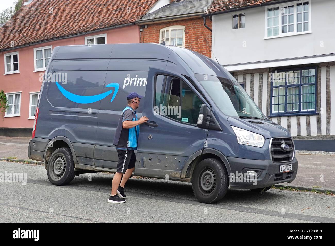 Chauffeur de livraison principal retournant à Ford Amazon van complétant la livraison de colis à la maison résidentielle du village avec le logo de la marque de publicité latérale Angleterre Royaume-Uni Banque D'Images