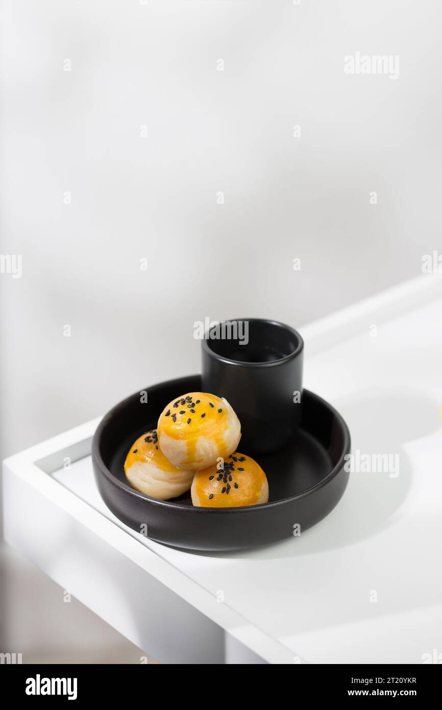 Pâtisserie chinoise parsemée de graines de sésame noires sur le dessus, et servie avec du thé chaud dans une tasse en céramique noire. Banque D'Images