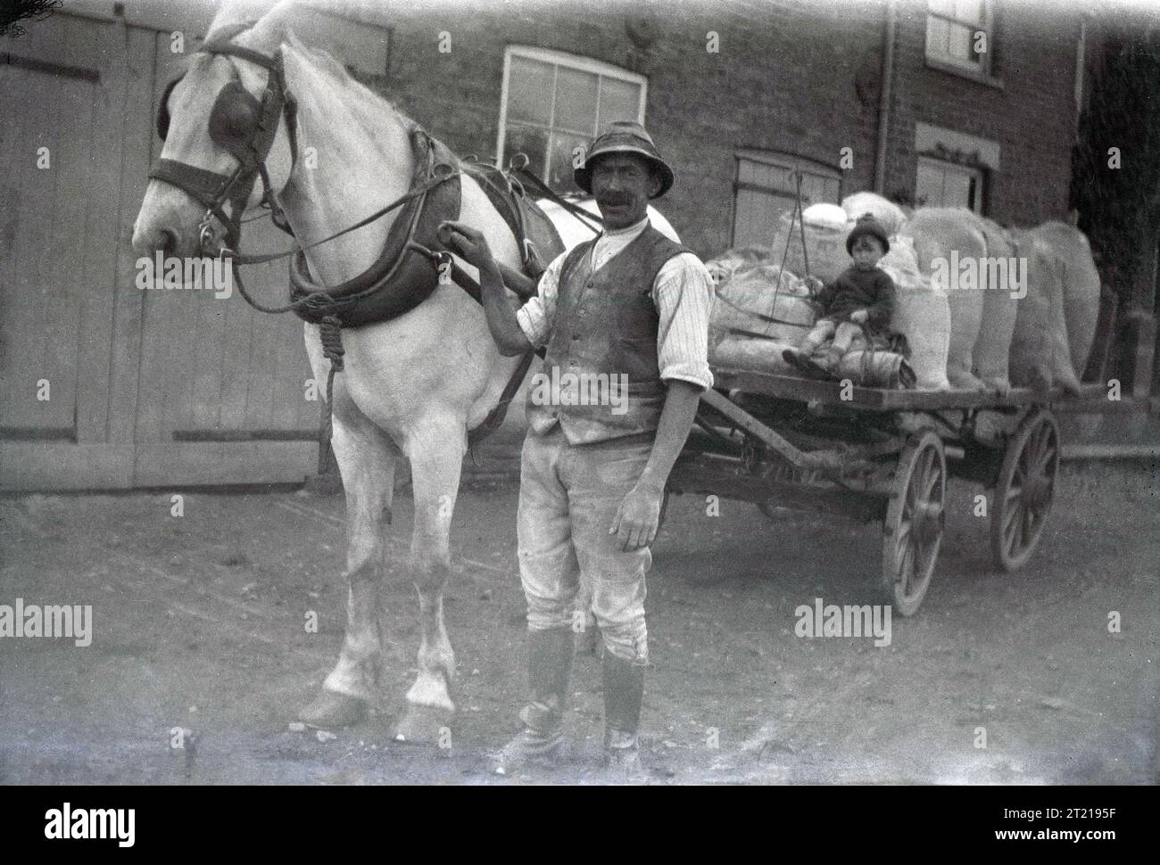 Années 1920, historique, un fermier debout avec son cheval & chariot en bois ouvert, avec un petit garçon assis près de sa cargaison de sacs de farine, Angleterre, Royaume-Uni. Banque D'Images