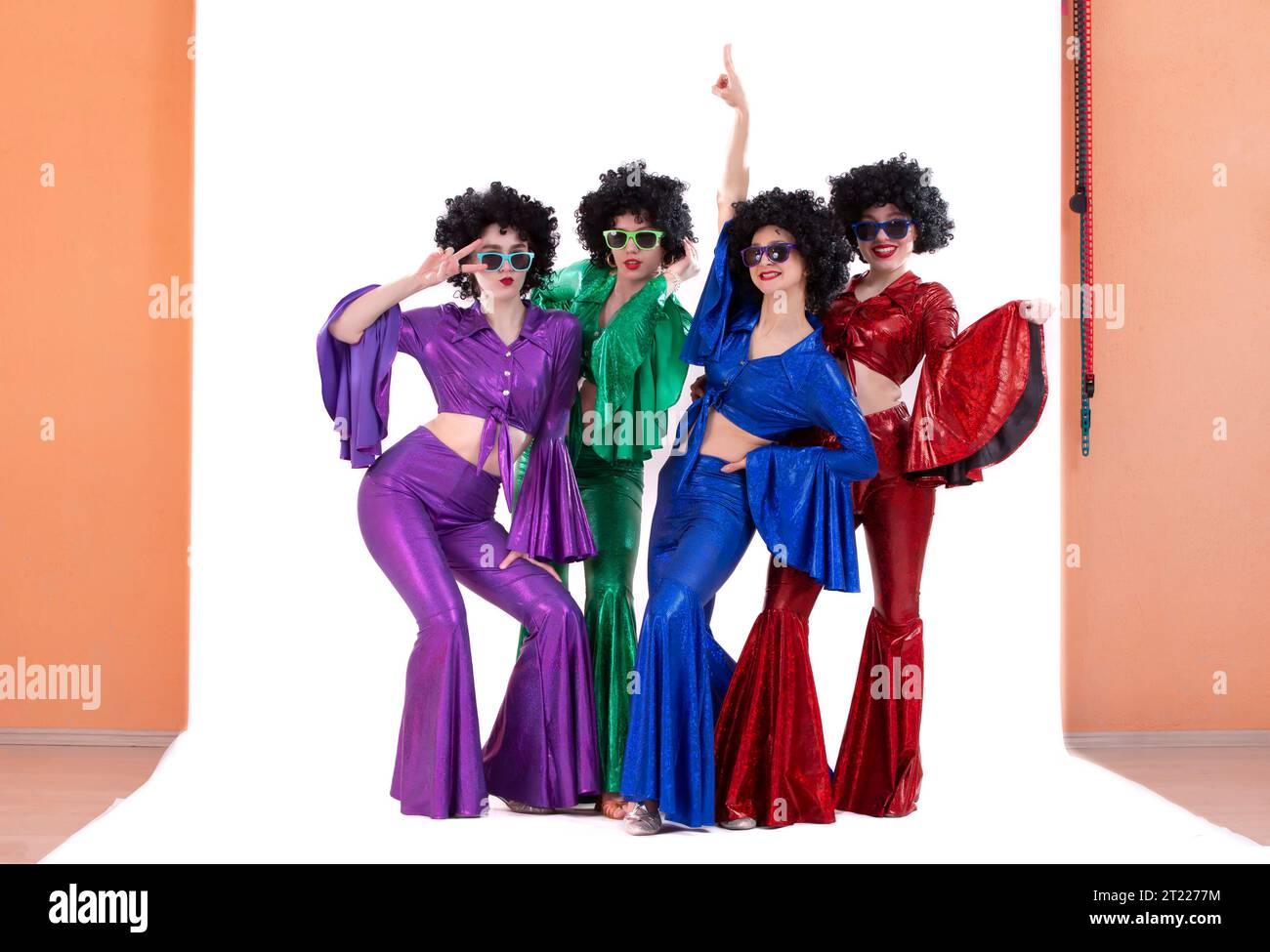 Un groupe de filles en costumes évasés colorés et perruques afro posent dans un studio photo. Style disco des années 80 ou 70. Banque D'Images
