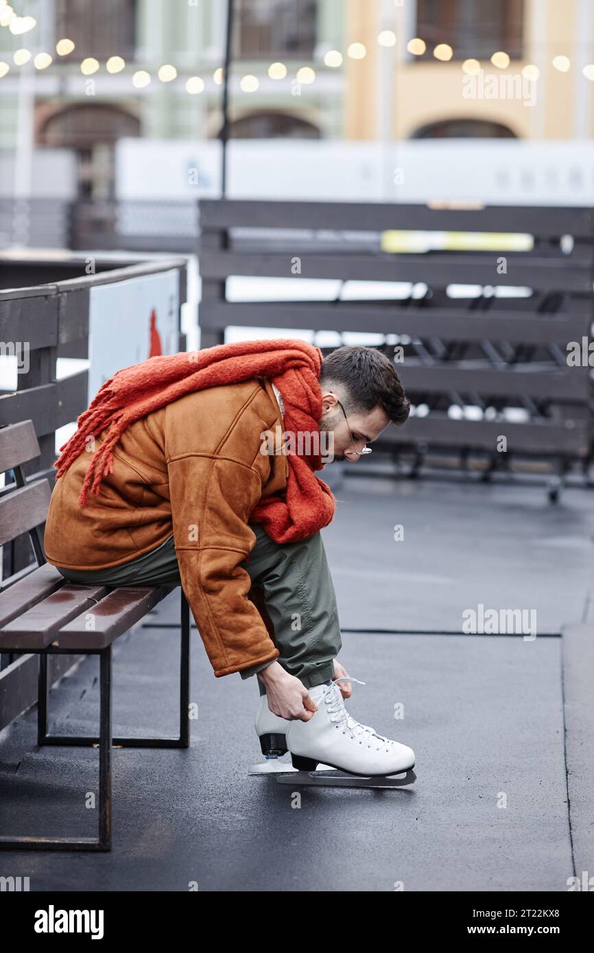 Portrait de vue latérale pleine longueur d'homme mettant sur des patins dans la patinoire de patinage à l'extérieur Banque D'Images