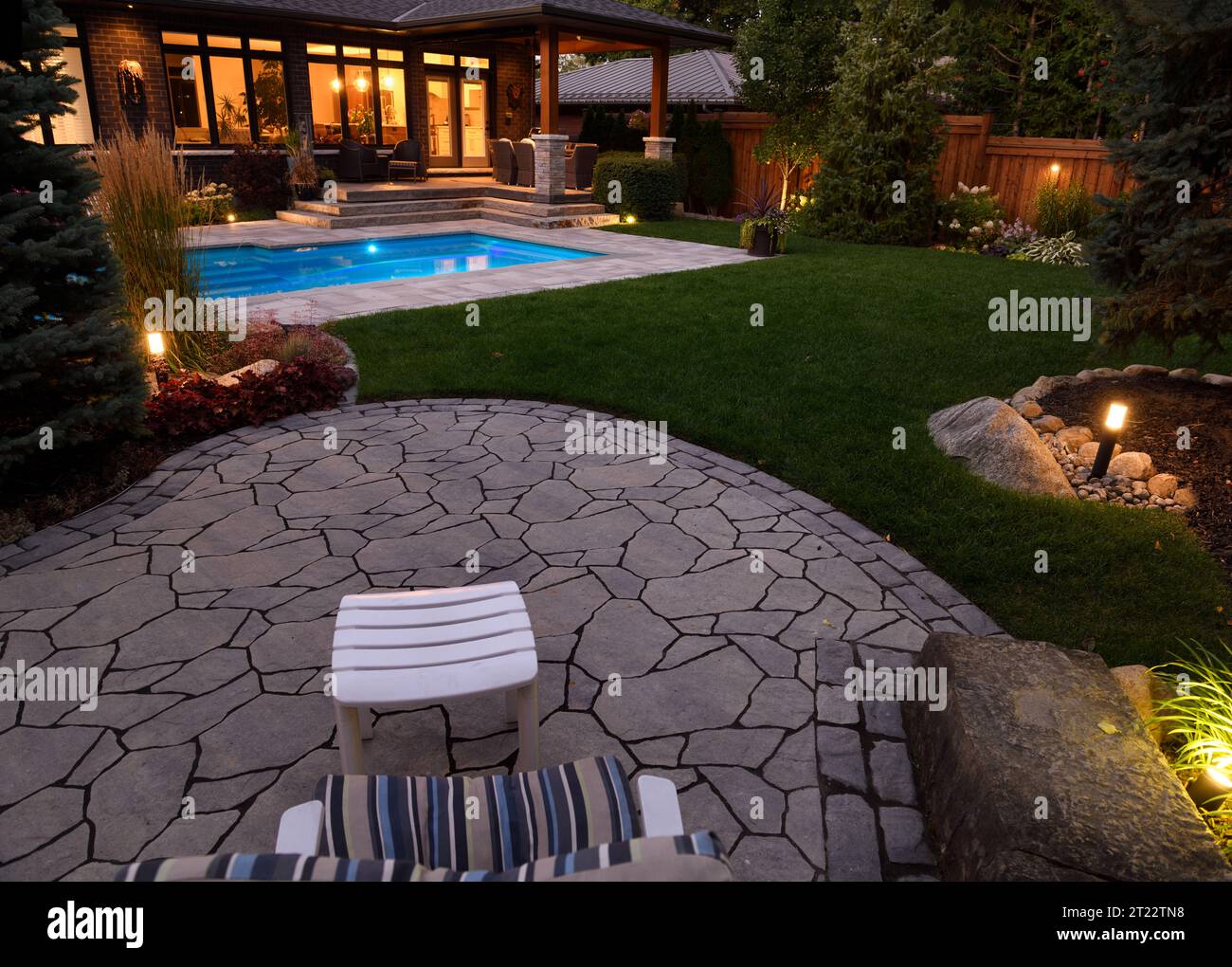 Maison avec patio extérieur coin salon et lumières allumées la nuit et piscine bleue éclairée avec terrasse en pierre Banque D'Images