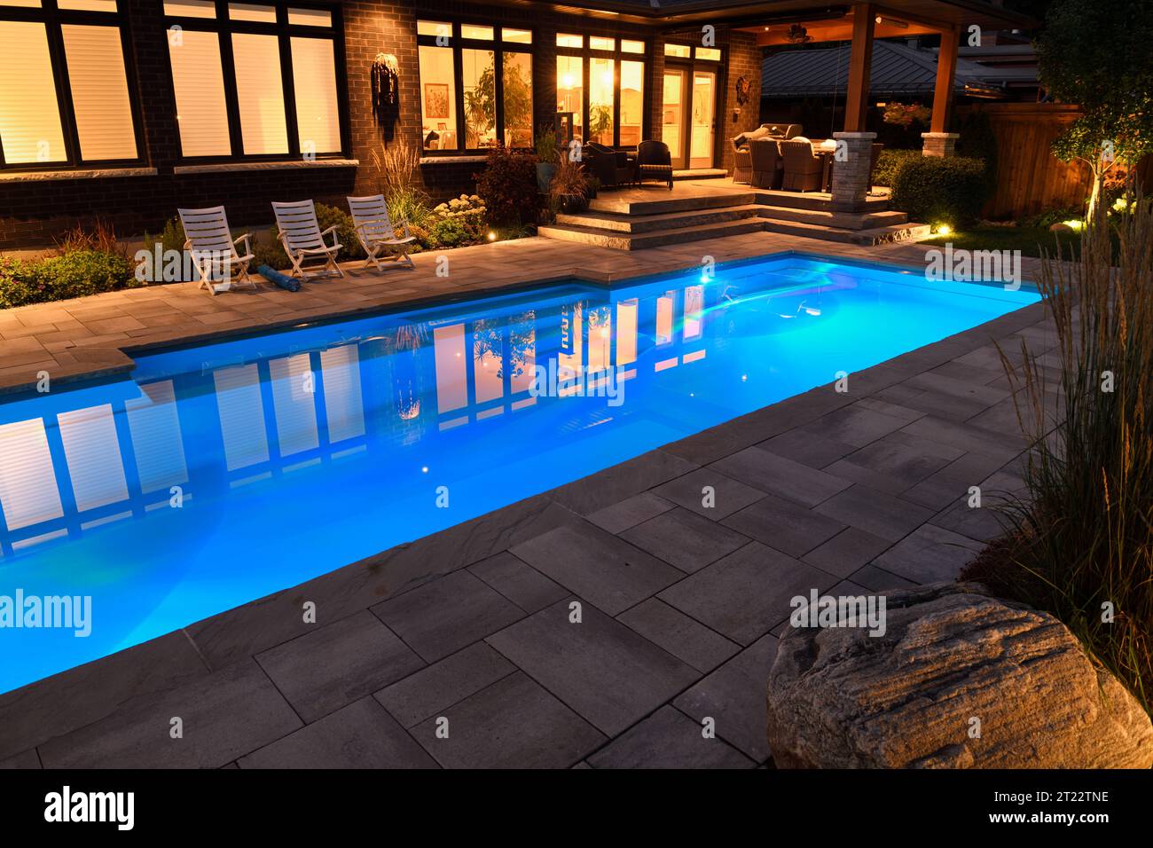 Maison avec patio extérieur et lumières allumées la nuit et piscine bleue éclairée avec terrasse en pierre Banque D'Images