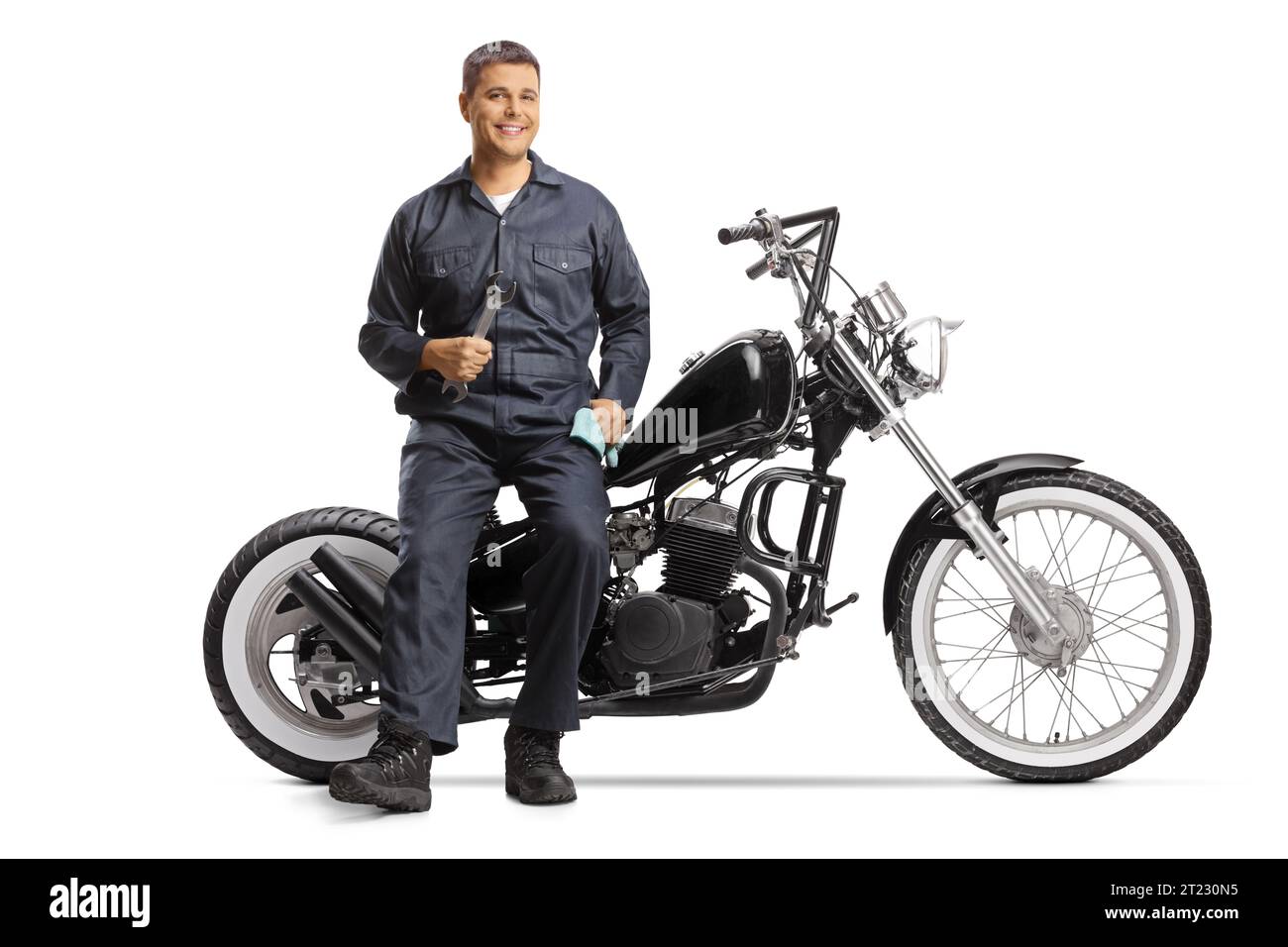 Mécanicien assis sur une moto et souriant isolé sur fond blanc Banque D'Images