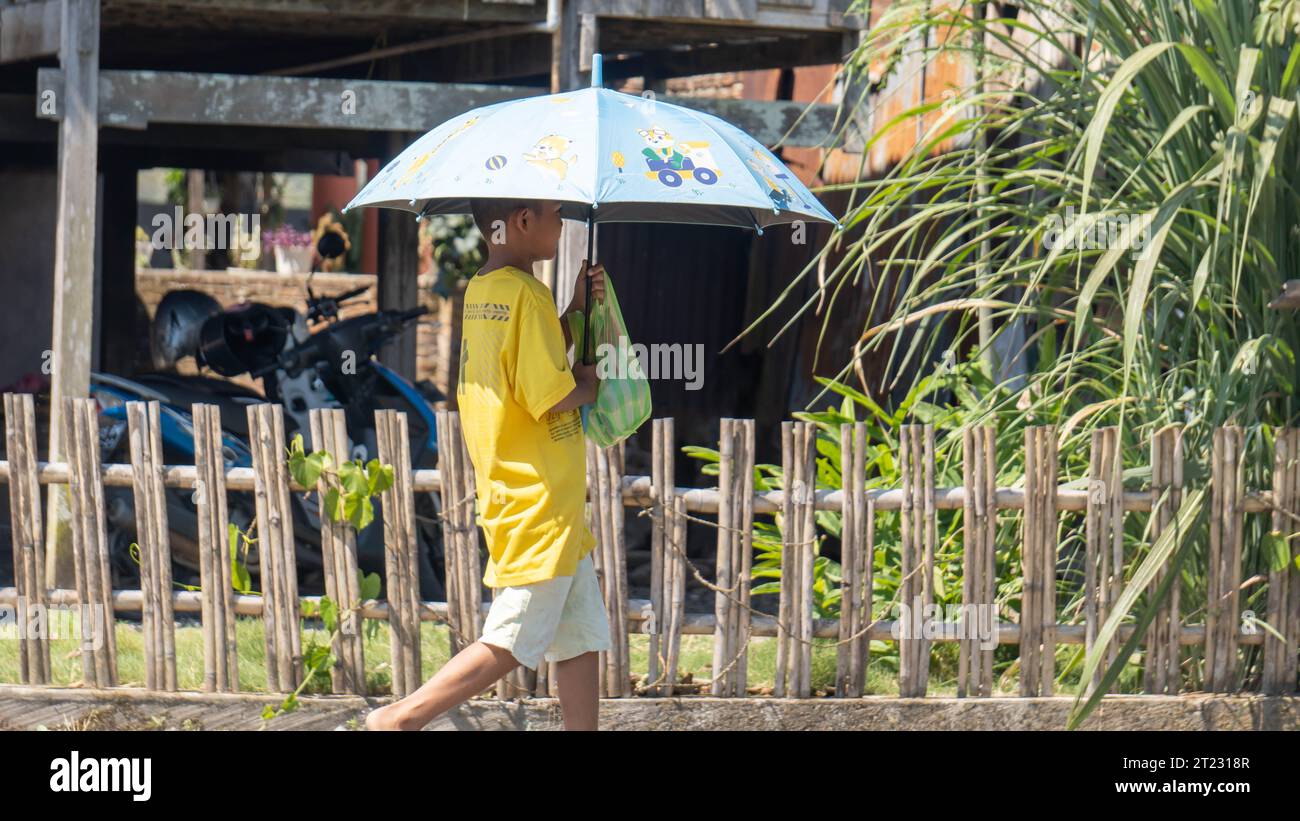 Pinrang Indonésie, 16 octobre 2023 : un garçon marche avec un parapluie sous le soleil brûlant. Après-midi dans le village de Masolo Pinrang, Indonésie Banque D'Images