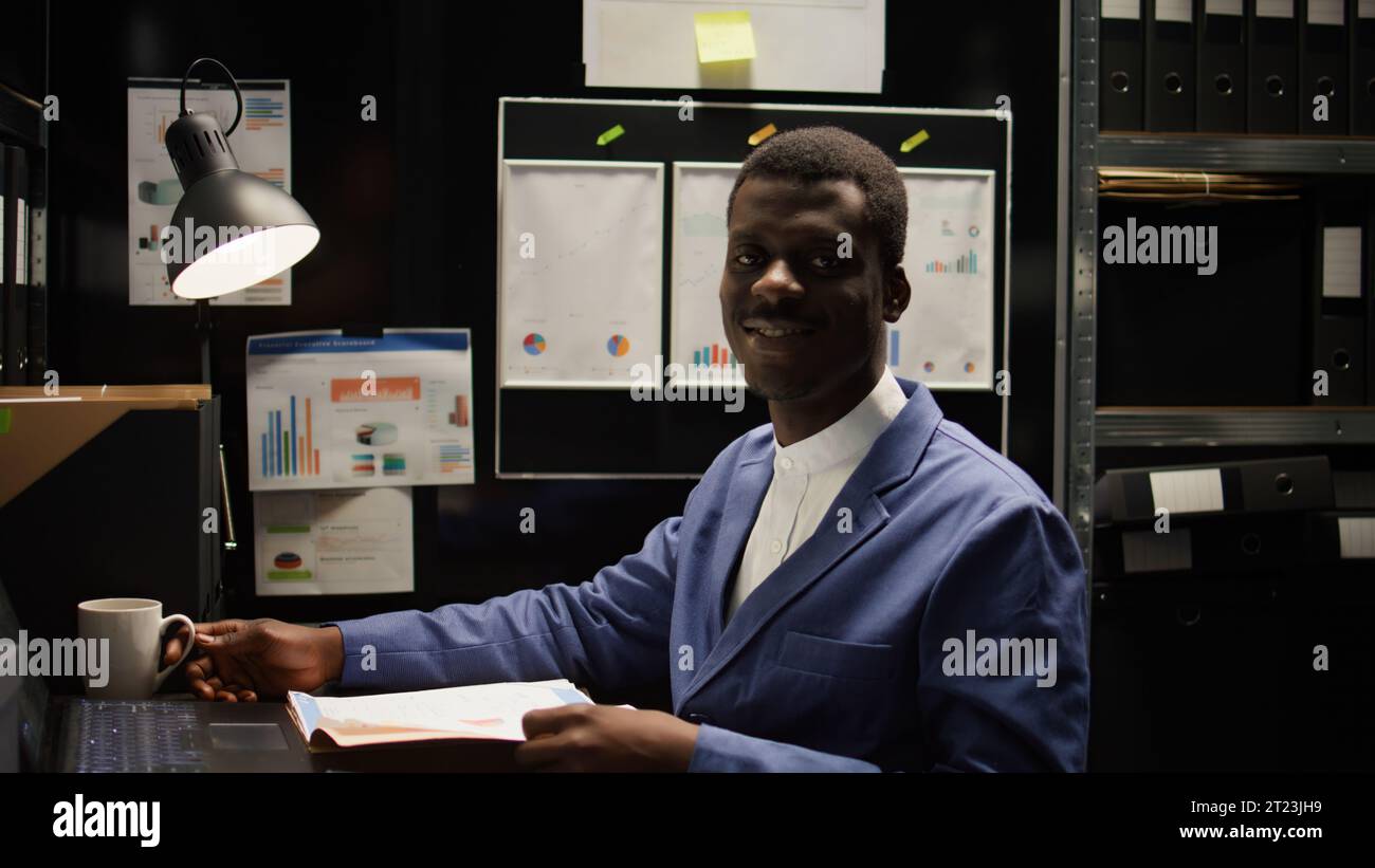 Sur le lieu de travail, détective afro-américain confiant entouré de documents et de preuves, prêt à résoudre les crimes et à rendre justice. Enquêteur privé analysant les dossiers et souriant à la caméra. Banque D'Images