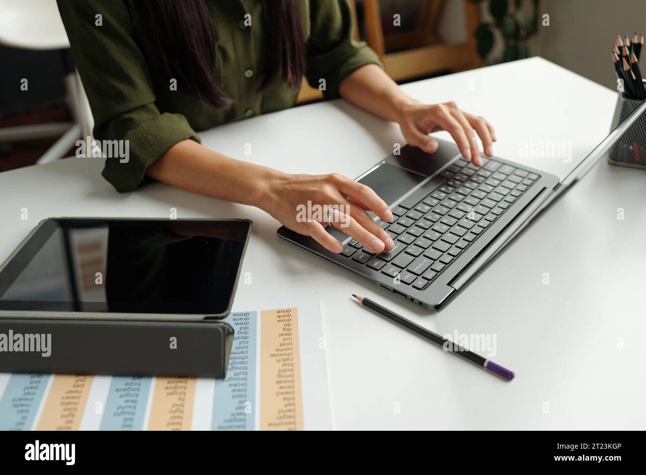 Mains de l'enseignant tapant sur le clavier d'ordinateur portable tout en étant assis par le bureau avec tablette et document avec les règles de grammaire et consultant les étudiants en ligne Banque D'Images