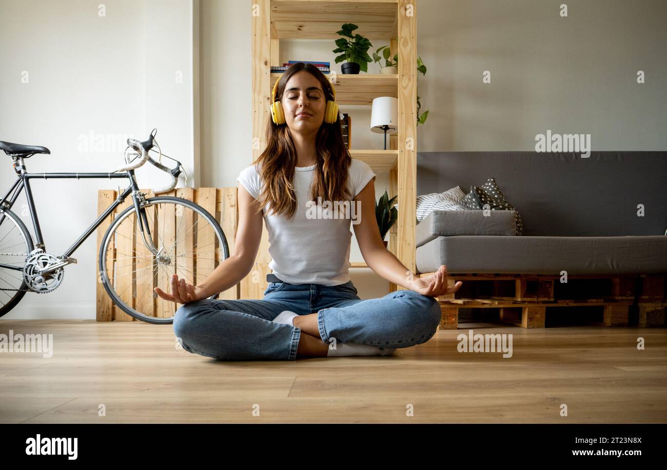 Jeune femme caucasienne faisant du yoga dans la pose de lotus et les yeux fermés dans un appartement. Détente et vie domestique Banque D'Images