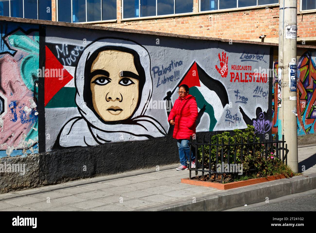 Une femme portant un manteau rouge passe devant une fresque montrant son soutien à une Palestine libre et exigeant la fin de l'holocauste palestinien, district de Miraflores, la Paz, Bolivie. La photo a été prise en septembre 2018. Banque D'Images