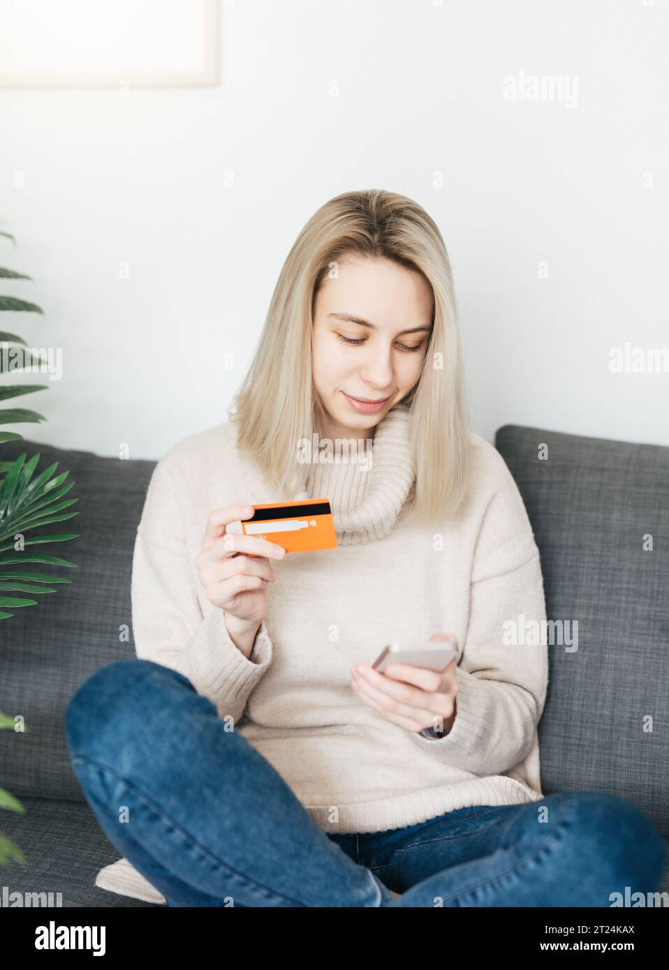 Jeune femme tenant un smartphone et une carte bancaire de crédit, impliquée dans le shopping mobile en ligne à la maison, heureuse femme achetant des biens ou des services Banque D'Images