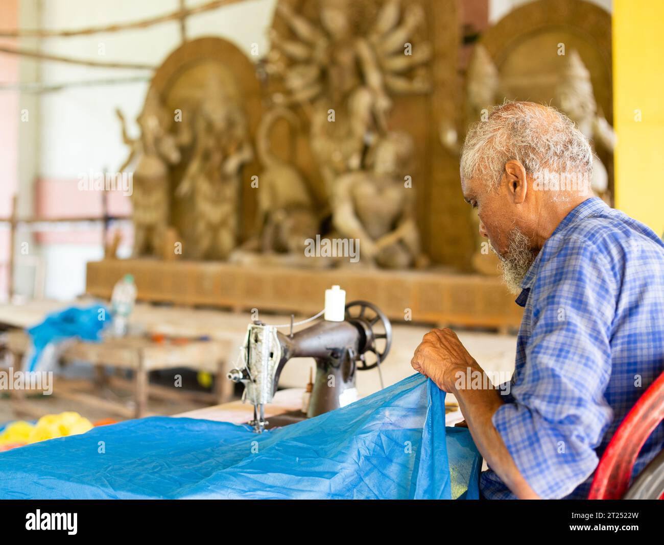 Birbhum, Bengale occidental, Inde - 14 octobre 2023 : un tailleur musulman piquant des vêtements de pandal devant l'idole durga avant le festival de puja hindou Banque D'Images
