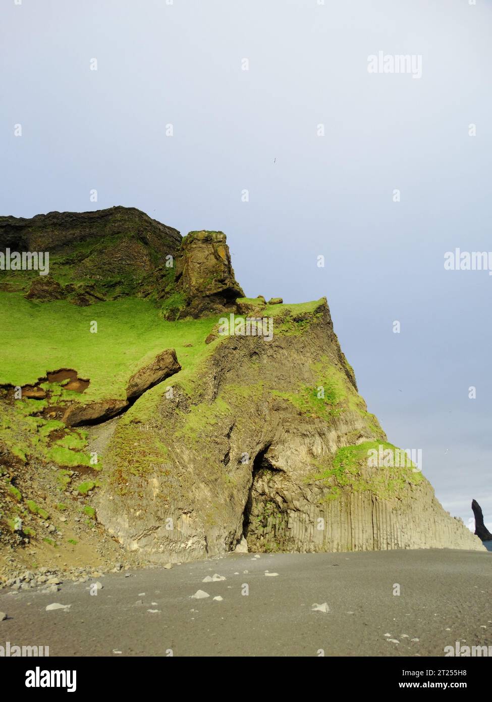 Une vue panoramique des falaises vertes sur un rivage rocheux noir par une journée nuageuse Banque D'Images