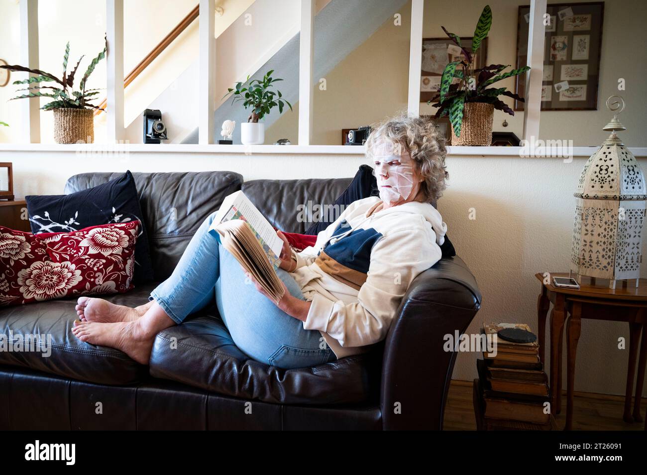 Femme mature lisant un livre à la maison portant un pack visage pour essayer de se débarrasser des rides indésirables et garder sa peau lisse Banque D'Images