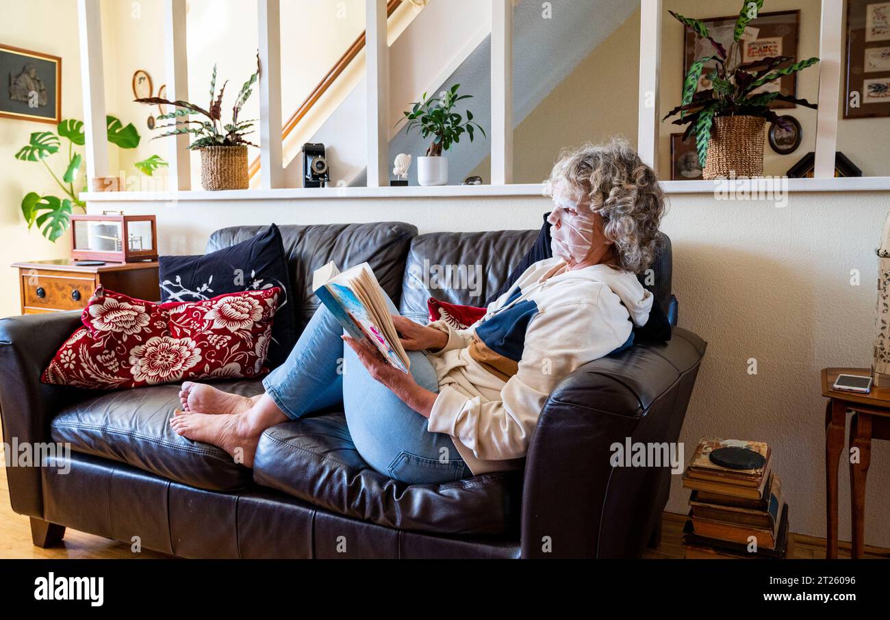 Femme mature lisant un livre à la maison portant un pack visage pour essayer de se débarrasser des rides indésirables et garder sa peau lisse Banque D'Images