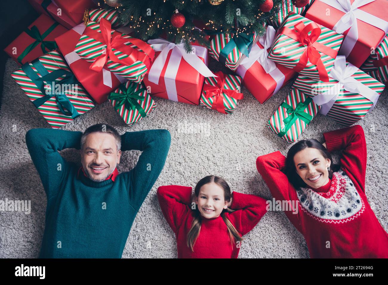 Ci-dessus, voir le portrait de la belle famille paisible petite fille parents couchés tapis plancher mains derrière la tête boîte cadeau arbre de nouvel an à l'intérieur Banque D'Images