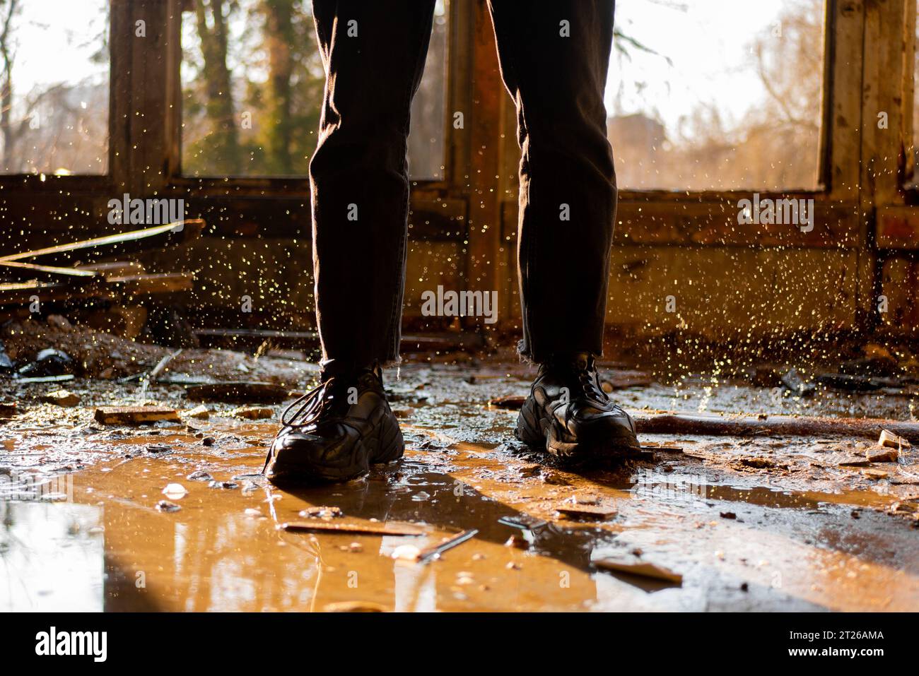 Jambes masculines en pantalon noir et baskets parmi la flaque d'eau et gouttes gelées dans une maison inondée, détruite et abandonnée. Rayons solaires. Banque D'Images