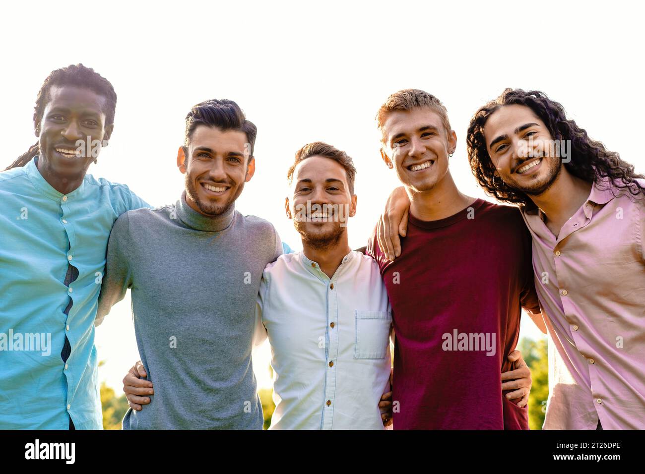 Un groupe multiracial de cinq amis masculins embrasse l'extérieur, partageant un moment d'unité et de joie. Ils sourient tous chaleureusement, dirigeant leur gai express Banque D'Images