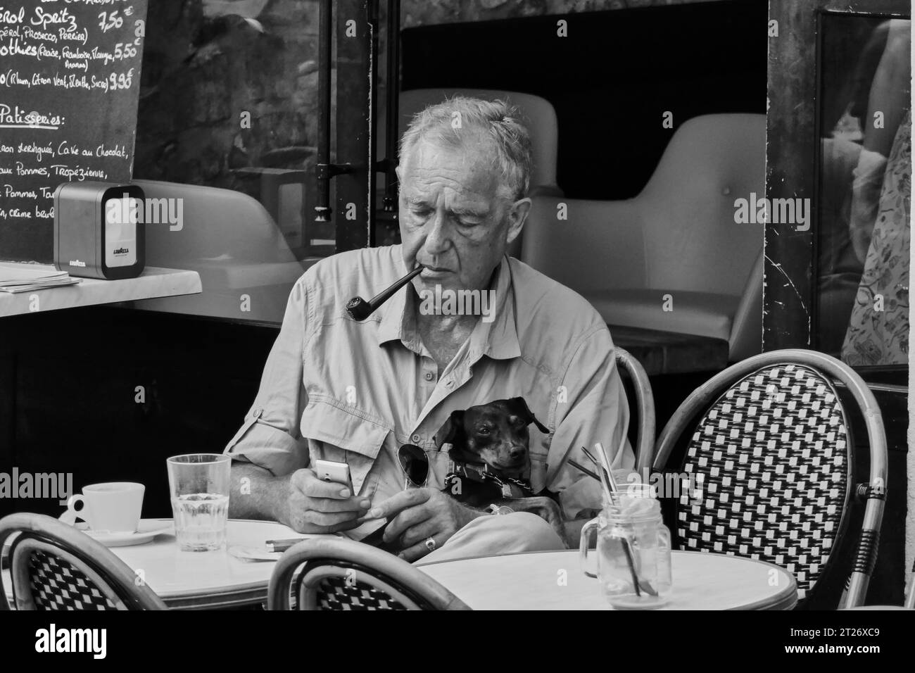 Personnage local fumant une pipe, assis dans un café avec son chien dans la vieille ville d'Antibes, France Banque D'Images