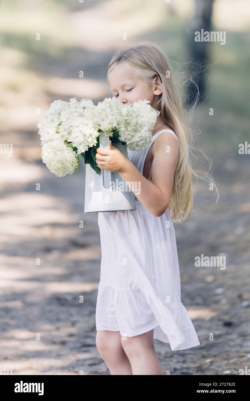 Portrait d'une jeune belle fille tenant un bouquet d'hortensias blanches dans ses mains. Regarde les fleurs. Cadre vertical. Banque D'Images