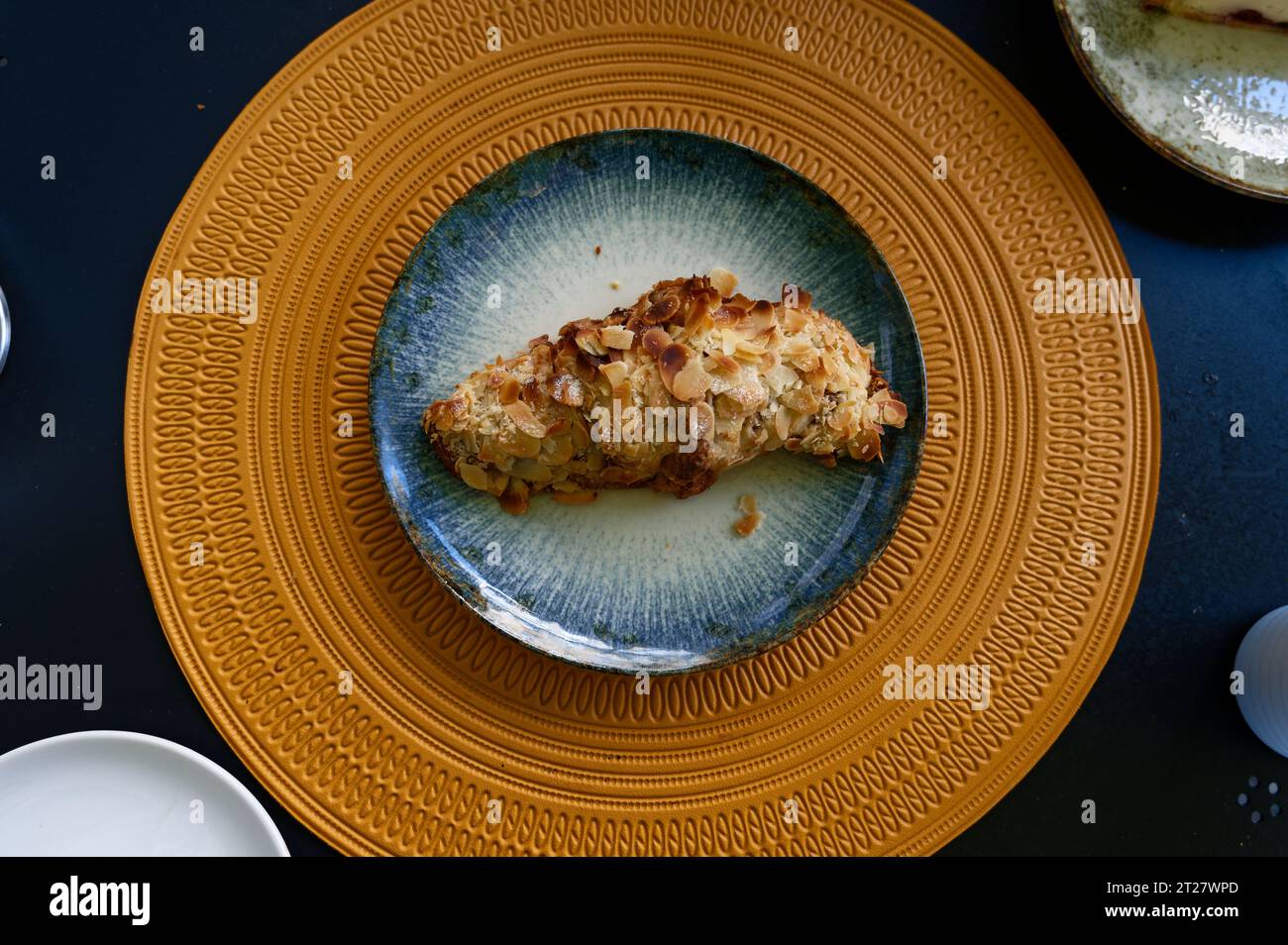 impressionnant croissant aux amandes sur une assiette bleue délavée reposant gracieusement sur une surface ornée jaune éclairée par le soleil Banque D'Images