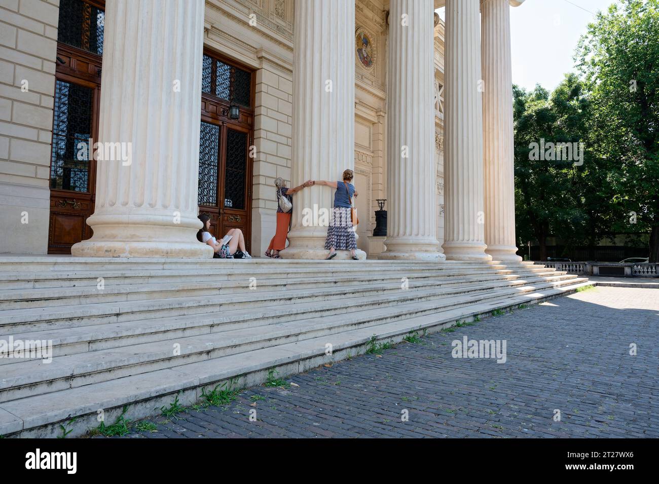 Les gens serrant un pilier dans l'athénée roumain, tandis qu'un adolescent est assis et lit Banque D'Images