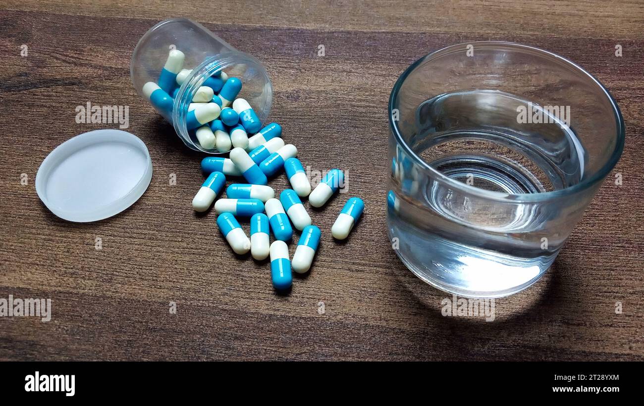 Un verre d'eau et des capsules médicales sur la table prêtes à être consommées. Compléments alimentaires, antibiotiques, vitamines. Banque D'Images