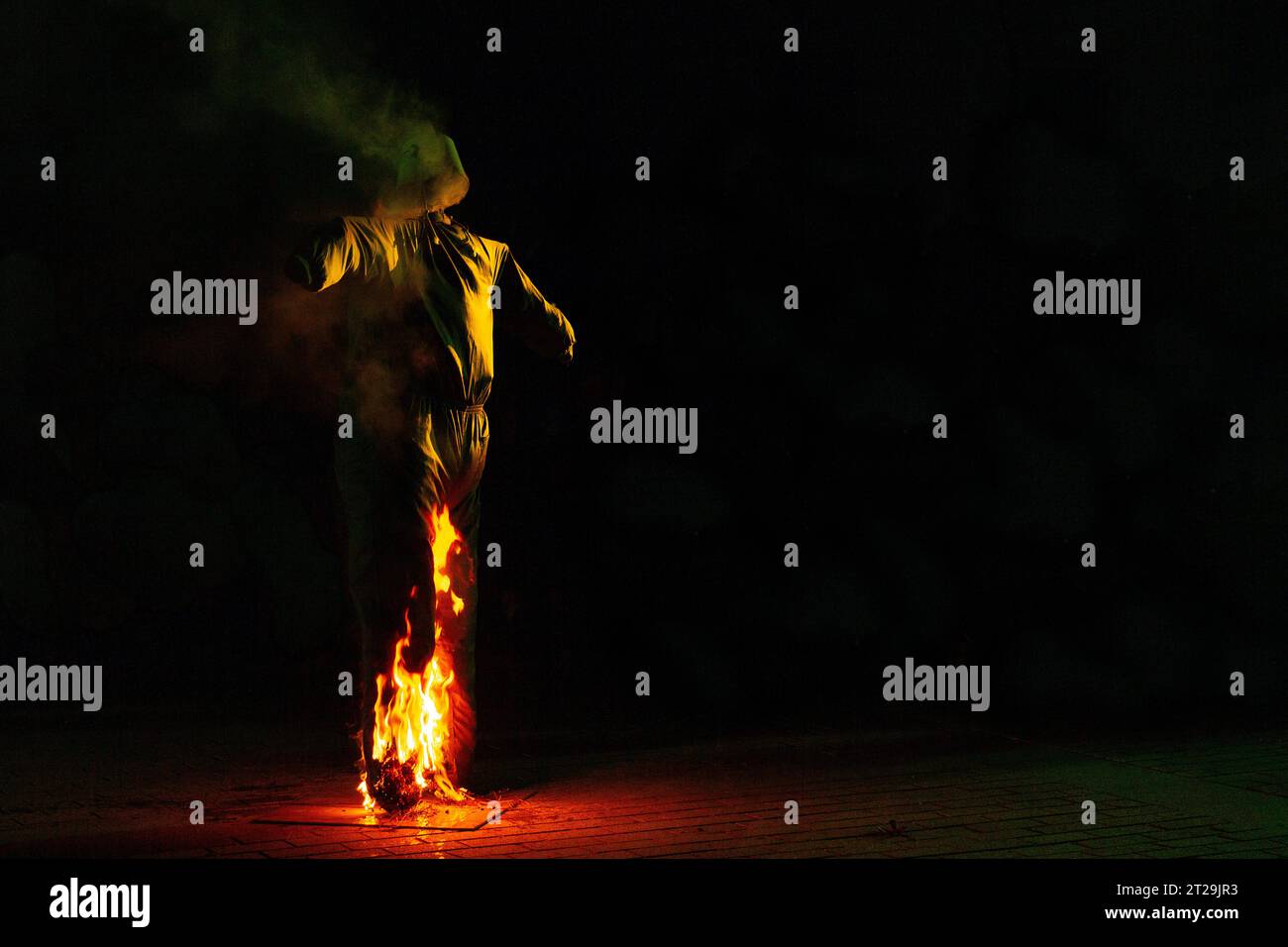 Des flammes brillantes s'élèvent et se déplacent autour de l'épouvantail à la nuit tombée dans un arrière-plan flou Banque D'Images