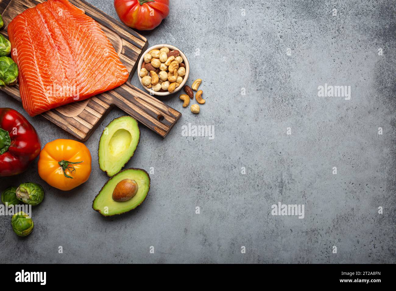 Filet de saumon frais cru sur planche à découper en bois, bio légumes et noix biologiques, vue sur le dessus de fond gris de pierre rustique. Ingrédients pleins de vitamines Banque D'Images