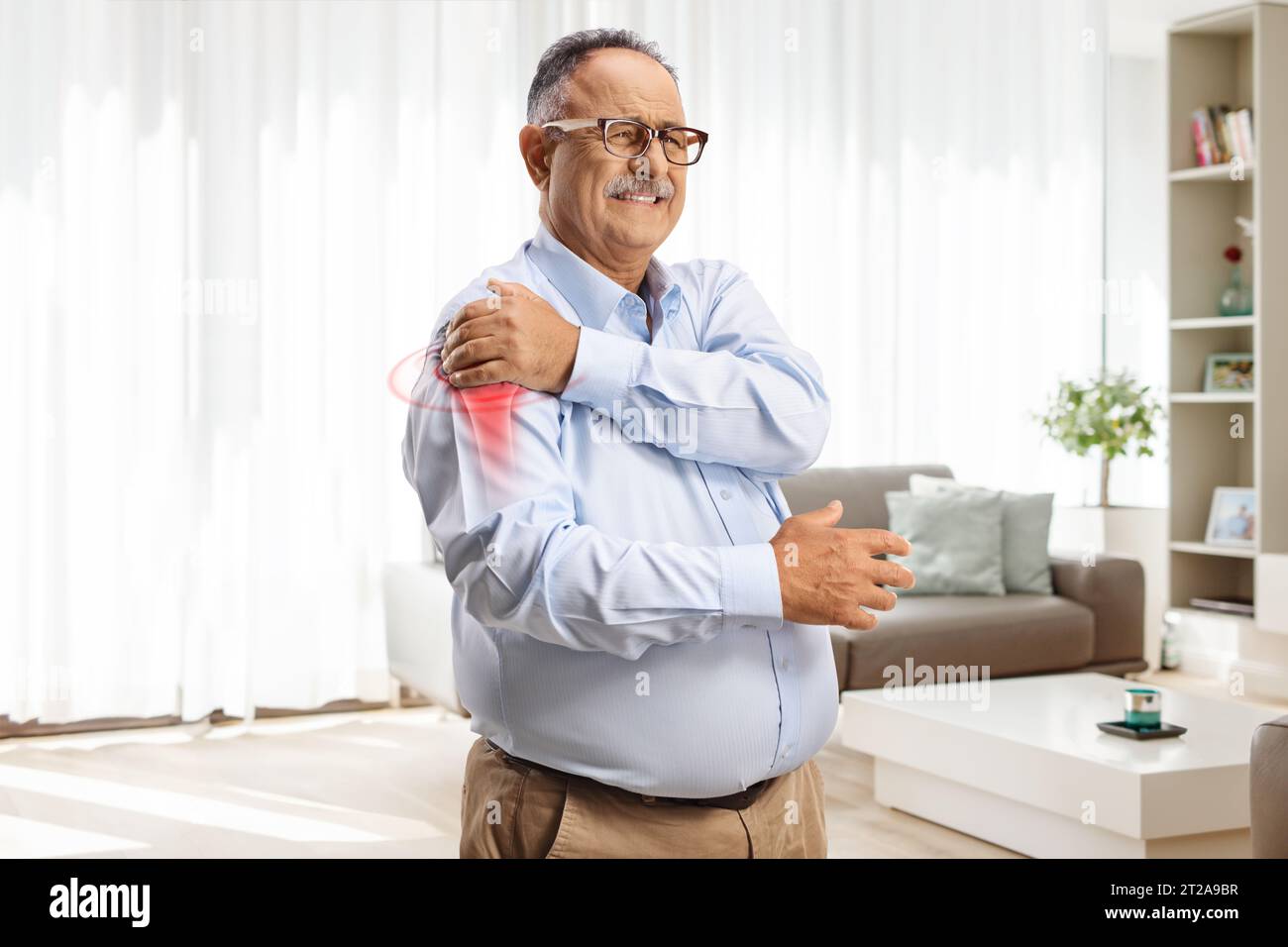Homme mature souffrant d'arthrite dans l'articulation de l'épaule tenant la tache rouge à la maison Banque D'Images