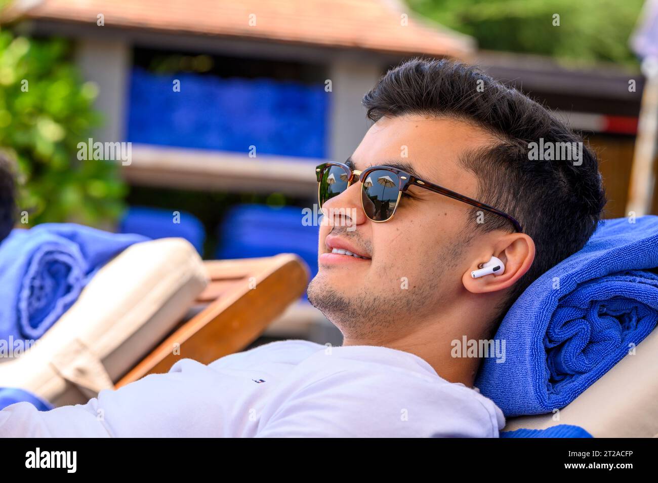 Un jeune homme d’une vingtaine d’années s’allonge sur un transat en écoutant de la musique avec AirPods dans un complexe hôtelier à Mui ne, au sud du Vietnam. Banque D'Images