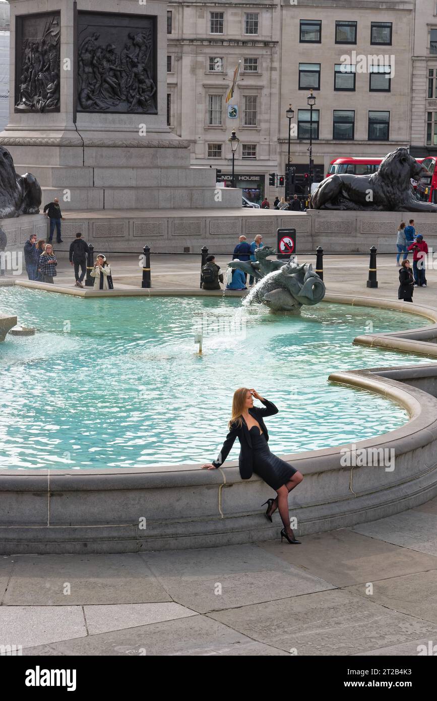 Une jeune femme européenne blanche séduisante dans une robe noire posant pour des photographies près de l'une des fontaines de Trafalgar Square, centre de Londres Angleterre Royaume-Uni Banque D'Images