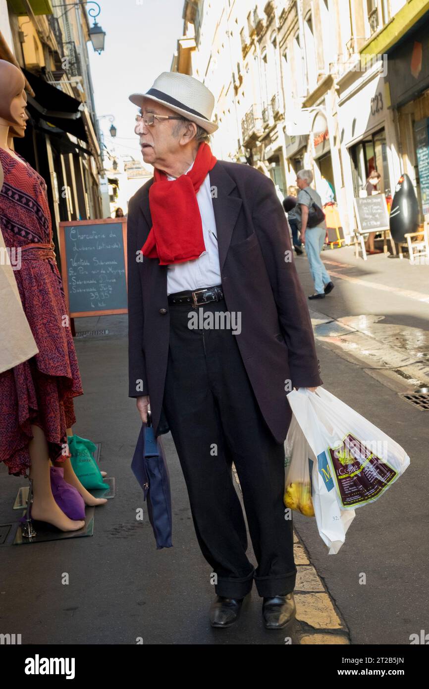 Un homme plus âgé portant un chapeau et une écharpe rouge magasinant dans la vieille ville, Aix-en-Provence, sud de la France. Banque D'Images