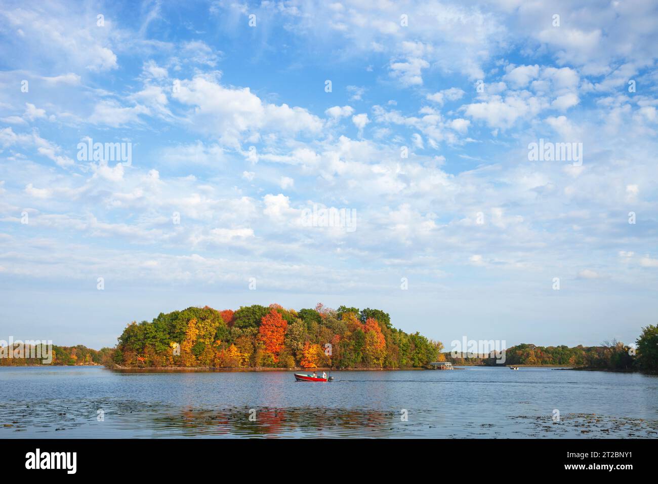 Père et fils en bateau de pêche sur un lac du Minnesota avec des arbres de couleur d'automne et de beaux nuages Banque D'Images