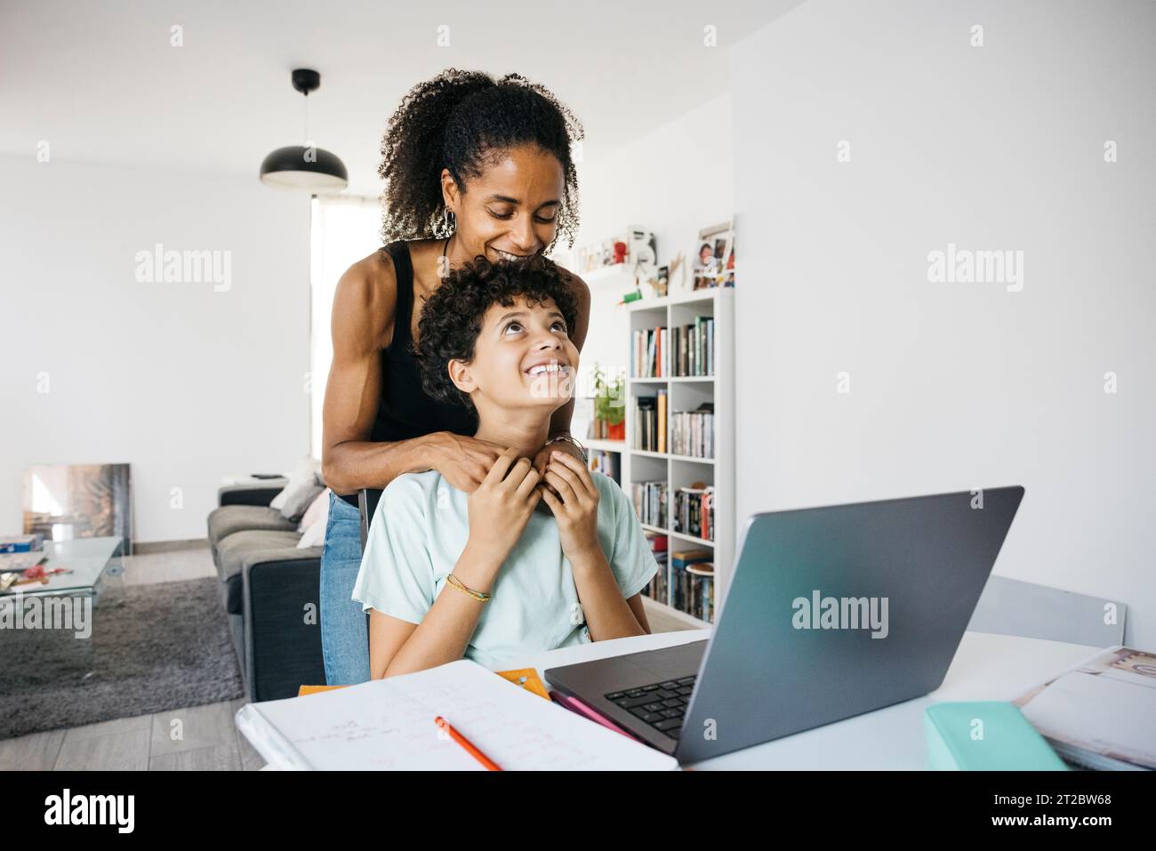 Femme joyeuse aidant sa fille à faire ses devoirs. Mère heureuse aidant sa fille avec les devoirs scolaires dans le salon. Banque D'Images