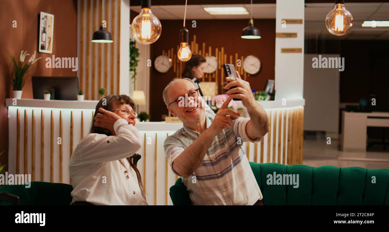 Personnes âgées prenant des photos dans le hall, enregistrant toutes les activités pendant les vacances de retraite à l'étranger. Vieux mari et femme prennent des photos sur smartphone, faisant des souvenirs pour les membres de la famille. Banque D'Images