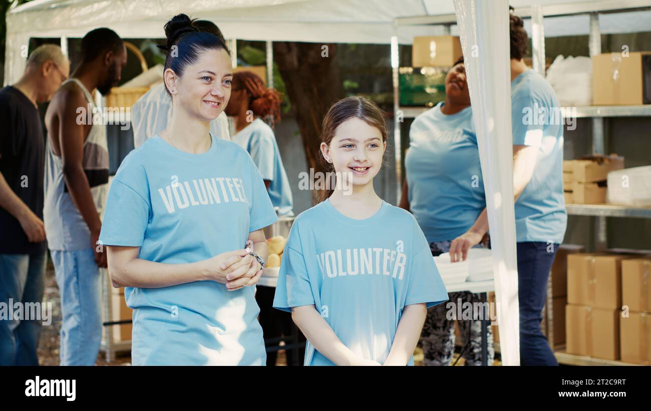 Portrait en vue latérale d'une mère et de sa fille en soutien à une campagne extérieure de banque alimentaire pour lutter contre la faim. Deux femmes caucasiennes portant des t-shirts bénévoles bleus sont prêtes à aider les sans-abri. Banque D'Images