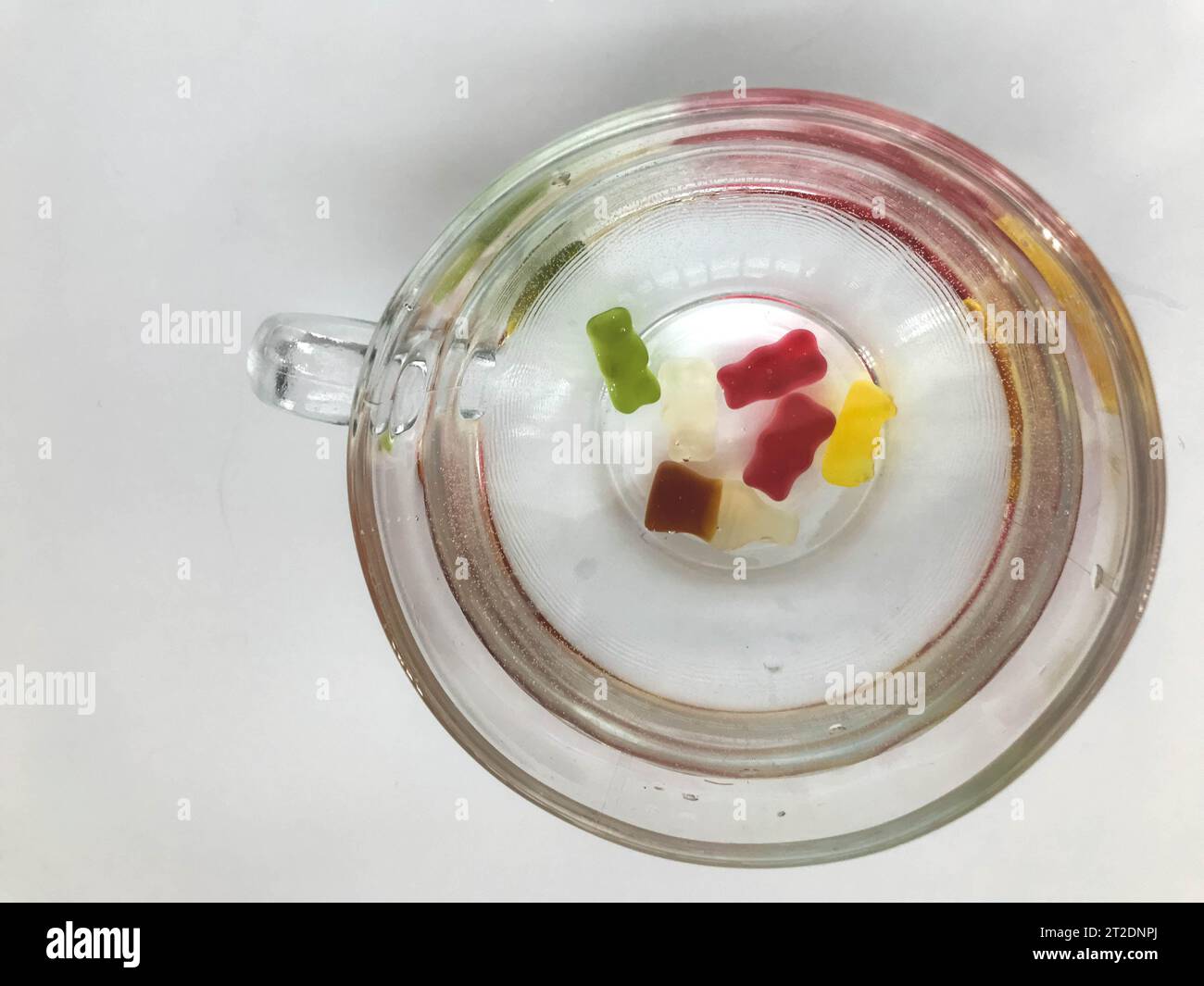 mug transparent, rond et grand, rempli d'eau. au fond de la tasse se trouvent des ours gommeux. les ours de couleurs jaune, rouge, vert nagent dans l'eau. m Banque D'Images