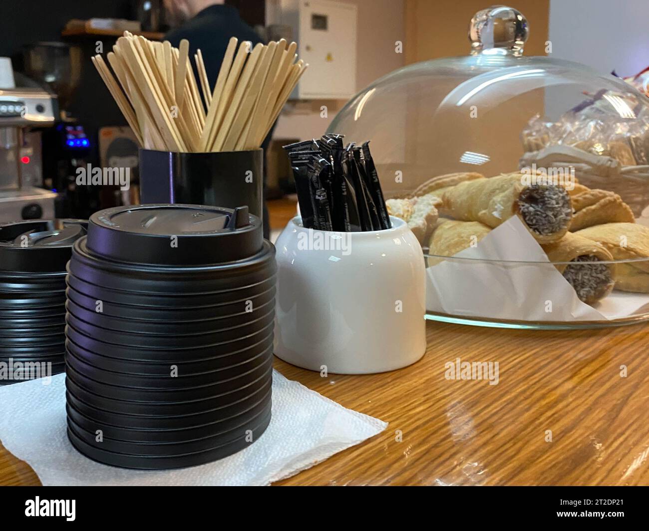 Bâtons jetables en bois naturel pour mélanger le sucre dans le thé ou le café, sucrier, couvercles thermo en plastique pour tasses et gâteaux sur le bar dans un petit café. Banque D'Images