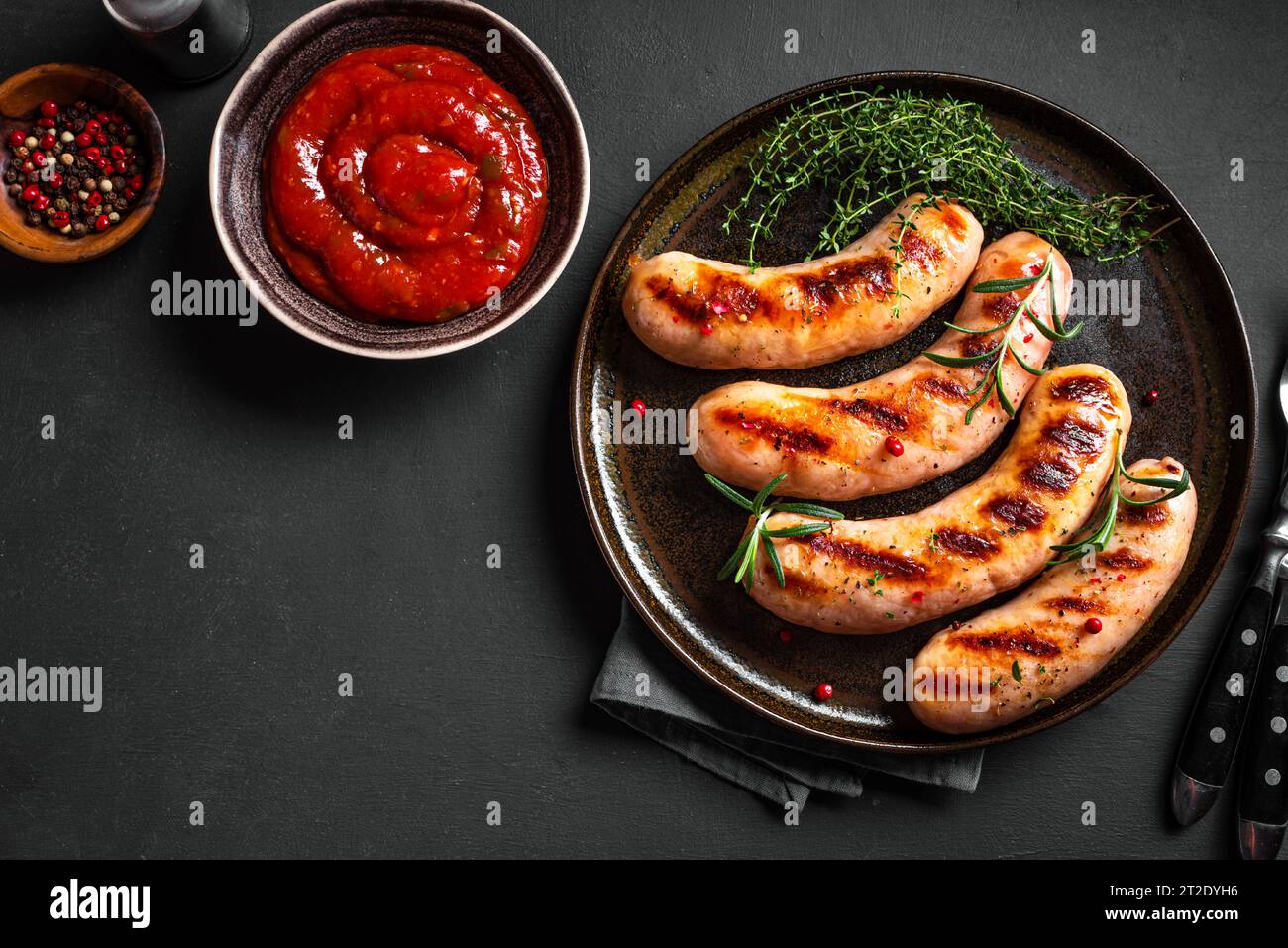 Saucisses grillées avec sauce tomate et herbes sur fond noir, vue de dessus, espace de copie. Saucisses wurst rôties maison sur assiette. Banque D'Images