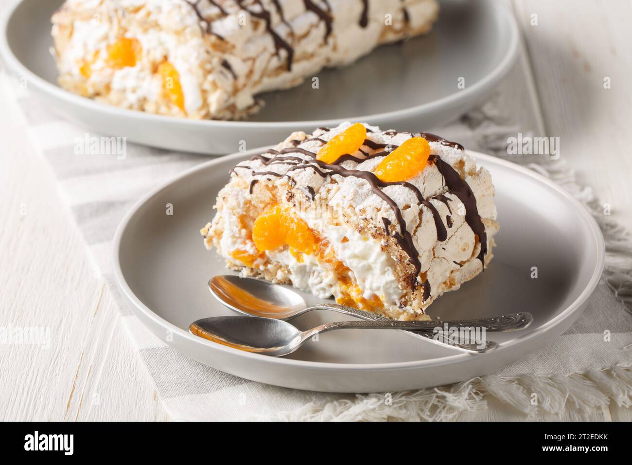 Délicieux dessert suédois maison gâteau roulé Budapest rempli de crème fouettée et mandarines en gros plan dans une assiette sur la table. Horizontal Banque D'Images