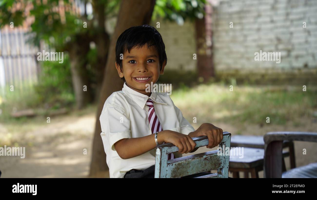 Portrait de joyeux enfant d'école indienne ou des enfants en uniforme levant la main dans la salle de classe tout en étudiant avec des livres et un ordinateur portable. Apprentissage en ligne Banque D'Images