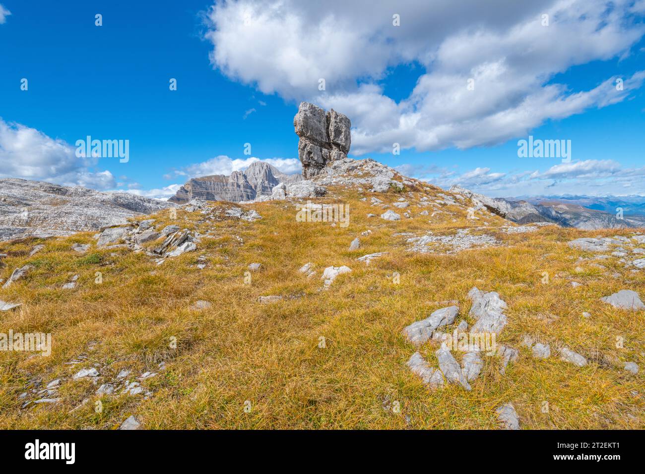 Grand rocher de calcaire autoportant au sommet d'une petite colline couverte d'herbe d'automne brune, contre un ciel bleu avec des nuages Banque D'Images