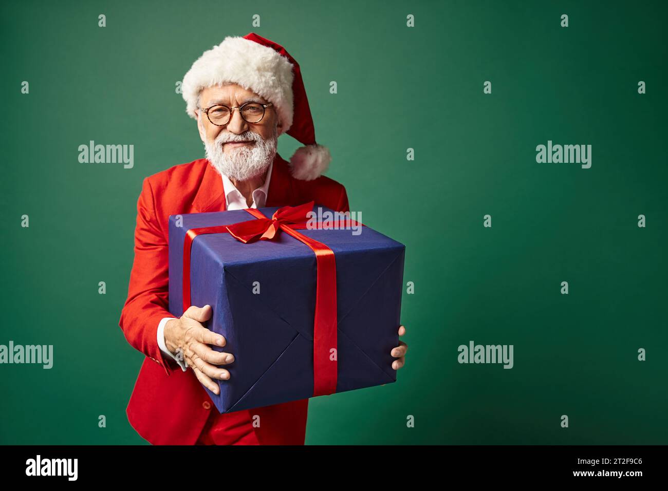 bel homme élégant dans le chapeau rouge de noël et des lunettes tenant un énorme cadeau bleu, concept d'hiver Banque D'Images